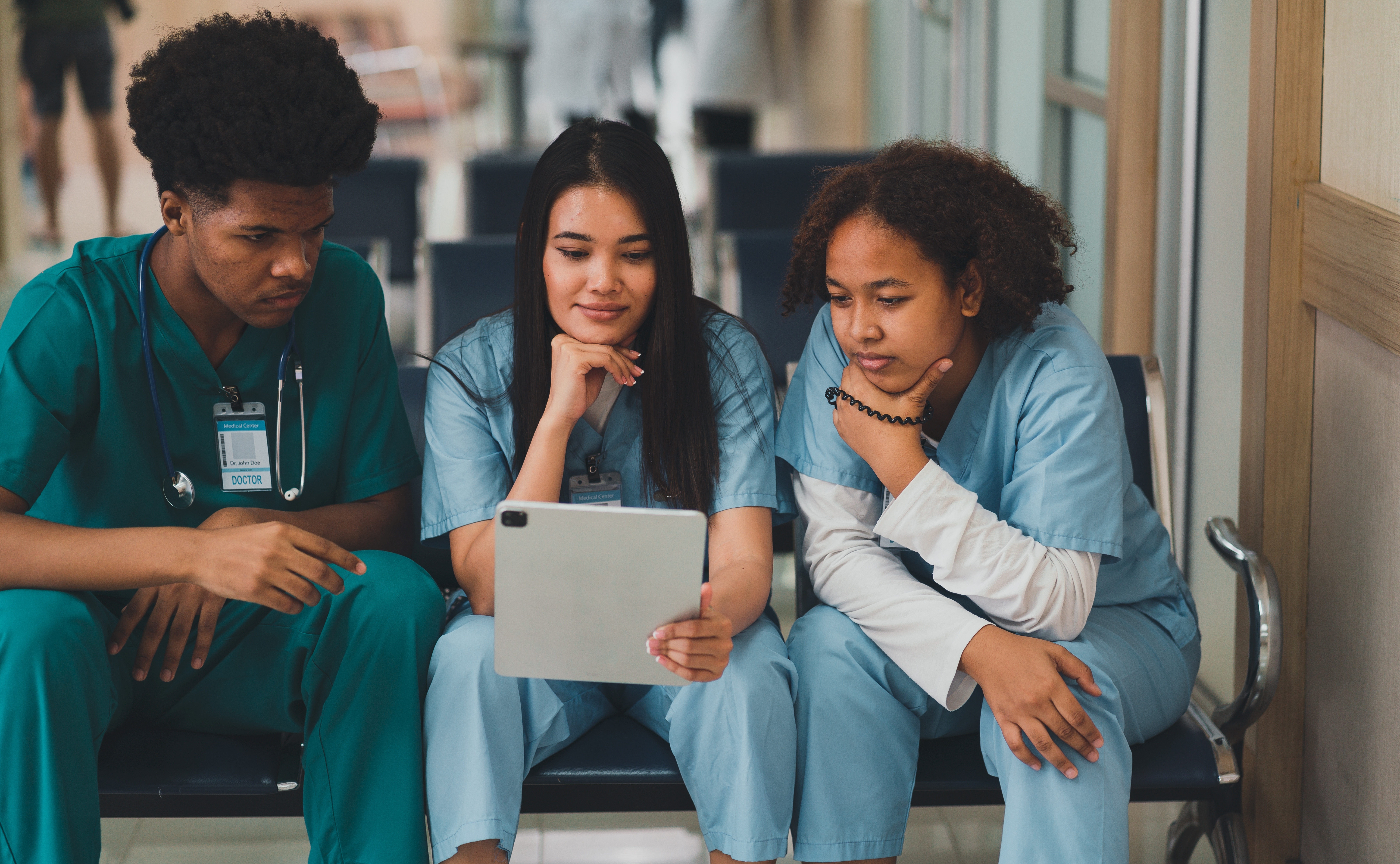 3 nurses in uniform sit closely together, looking at a shared screen. They are learning together.
