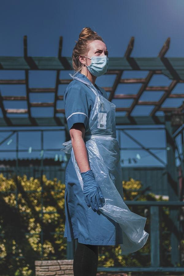 a nurse in blue uniform and full PPE stands powerfully outside looking into the distance