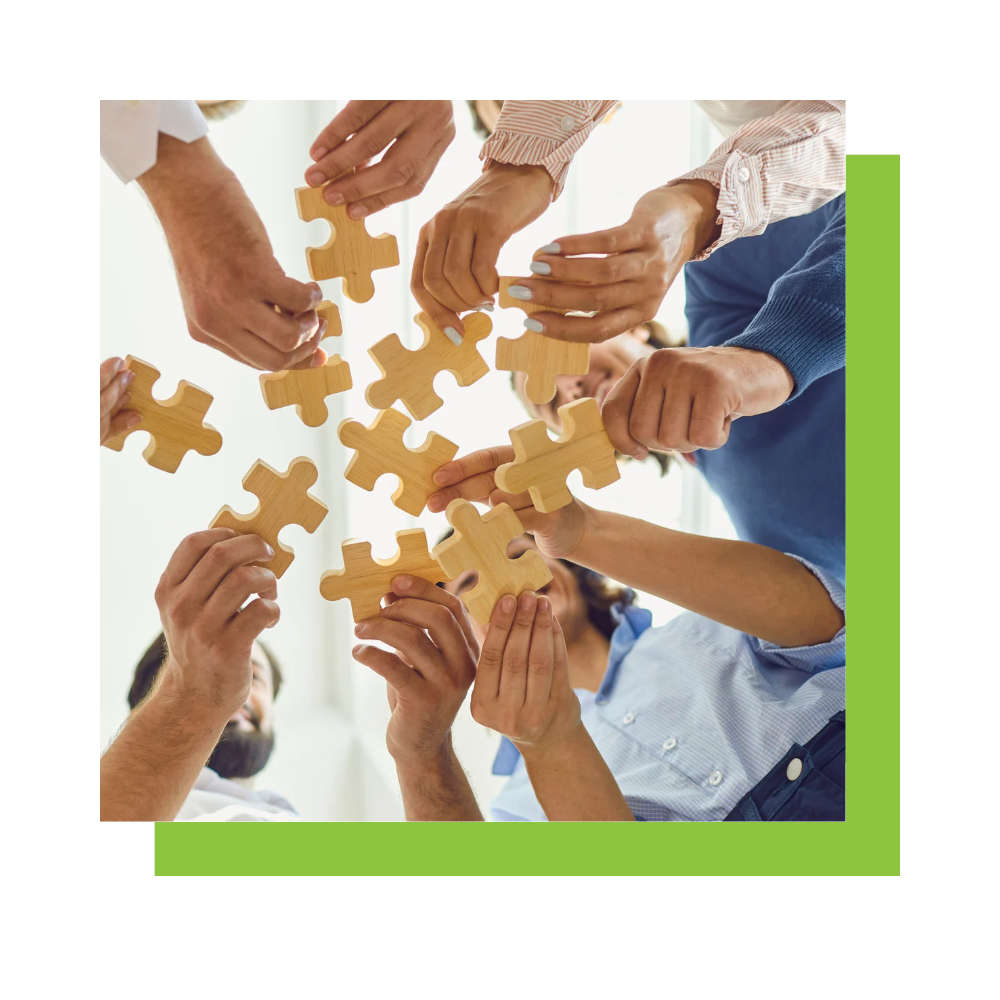 A group of people hold together pieces of a jigsaw puzzle. Underneath the square image is a green frame